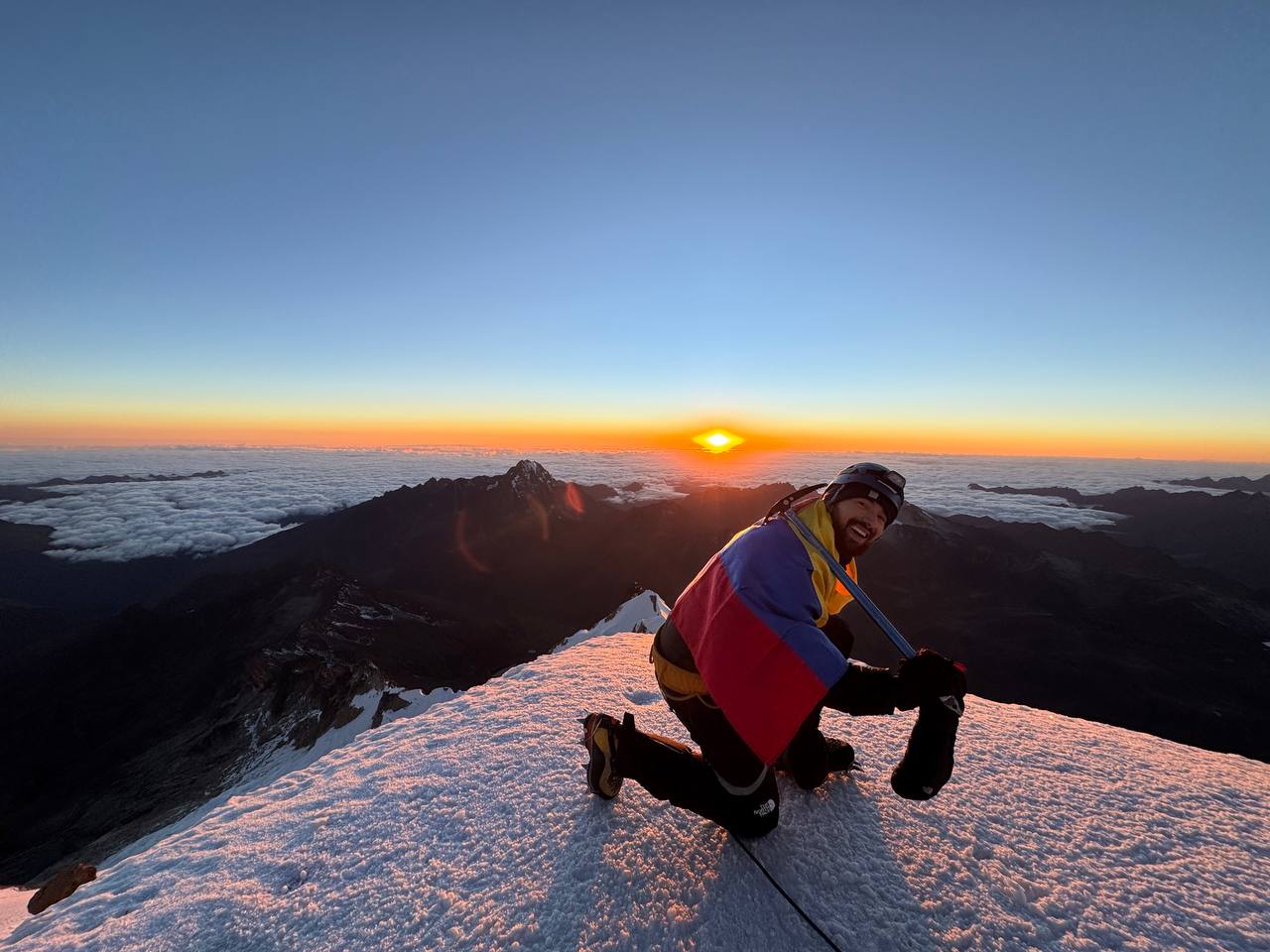 Andrés en la cima de una montaña al amanecer con la bandera de Colombia